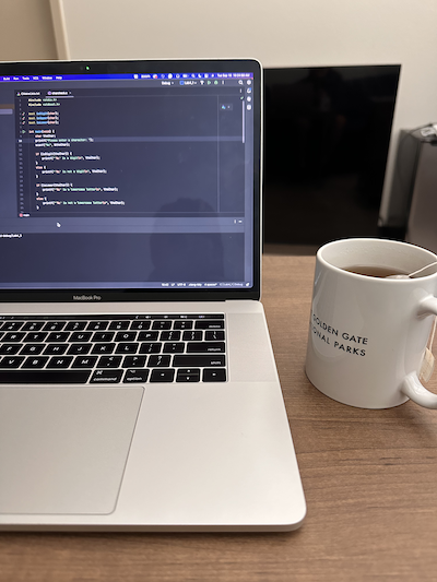 a laptop with C code next to a mug with tea in it