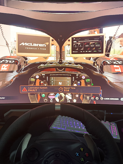 computer monitor showing the cockpit of an f1 car with a sim racing wheel in front